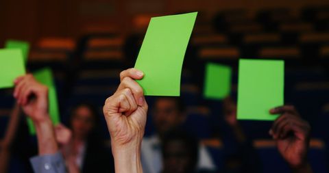Hands holding green cards for voting in decision-making process