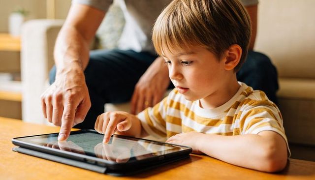 Young boy learning on tablet while parent guiding finger, concentrating on digital learning