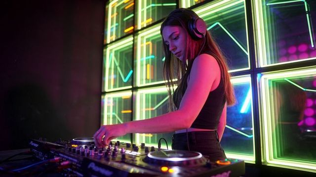 Female dj mixing on controller in neon-lit nightclub with led wall and modern headphones