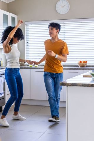 Interracial couple dancing joyfully in bright modern kitchen holding hands smiling