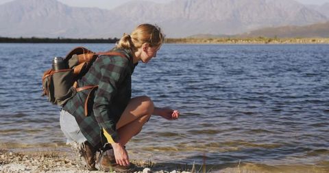 Adventurous Woman Hiker Touching Lake Water in Wild Landscape