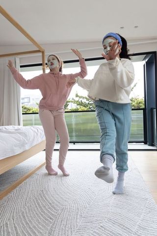 Teen friends dancing in pastel loungewear with facial masks in bright modern bedroom