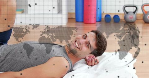 Smiling man resting after workout on mat with kettlebells and world map overlay