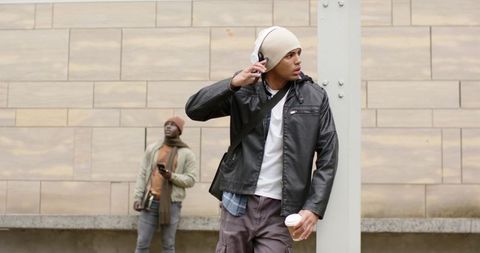 Young commuter adjusting headphones while holding takeaway coffee at urban plaza wall