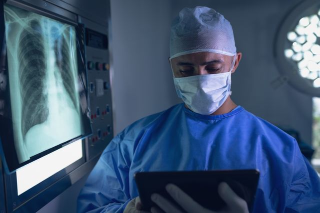 Surgeon in operating room wearing protective gear, examining x-ray on digital tablet. Useful for medical, healthcare, and technology themes. Ideal for illustrating modern medical practices, surgical procedures, and the use of digital technology in healthcare.