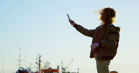Woman taking selfie at sunset with harbor in background