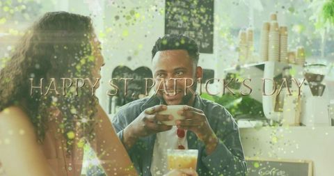 Smiling man holding cup, sipping coffee in festive st. Patrick's day cafe scene with green confetti