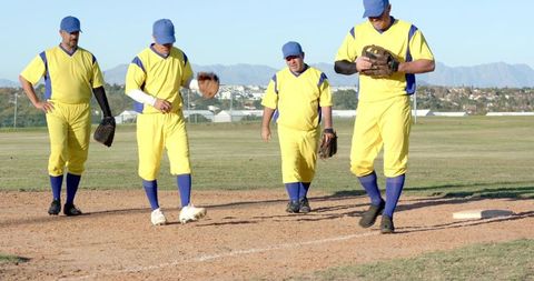 Mature male baseball teammates walking on diamond wearing bright yellow uniforms and blue caps