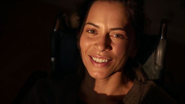 Smiling woman in wheelchair, warm low-light closeup portrait conveying resilience and hope