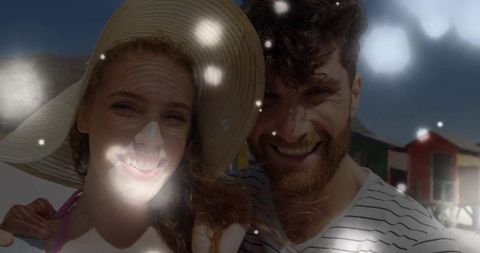 Smiling couple at beach with sunhat and colorful huts