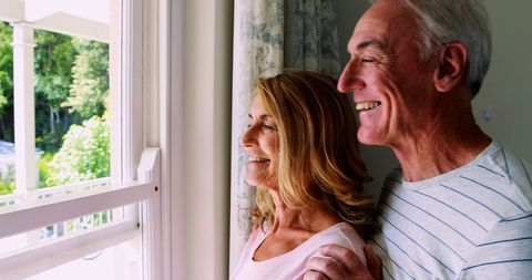 Happy Senior Couple Enjoying View from Window at Home