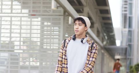 Asian commuter walking through transit corridor wearing beanie headphones backpack