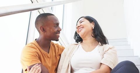 Smiling couple leaning on stair landing sharing warm moment in bright minimal interior