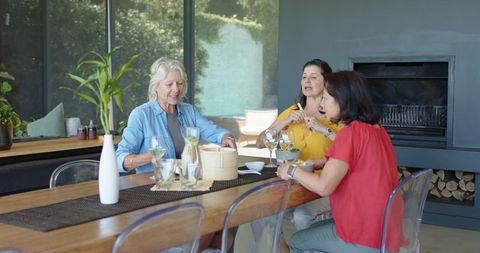 Women sharing sunny brunch, sipping lemon water and chatting around modern wooden dining table