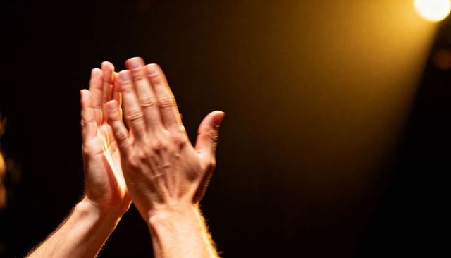 Applauding hands in warm spotlight on dark stage - theater applause and celebration