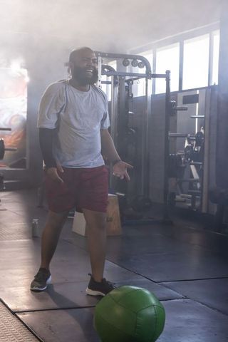 African american man training with green medicine ball in sunlit gym