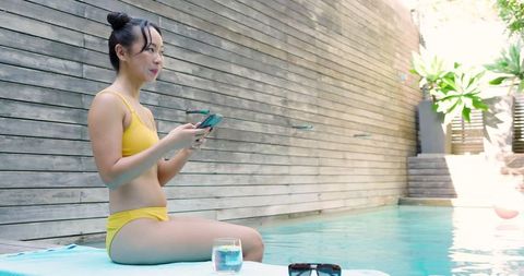 Woman Relaxing at Poolside Using Smartphone Outdoors