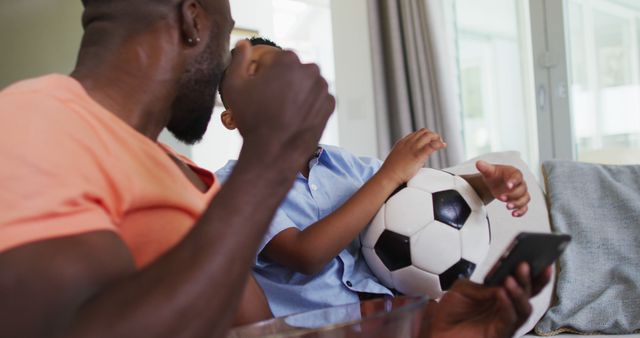 Father and son enjoying time together at home, holding a soccer ball and engaged in playful activity. Perfect for illustrating family bonding, parenting moments, or home leisure activities. Suitable for advertisements, family-oriented content, and educational materials on parenting.