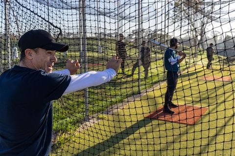 Baseball coach guiding youth players during sunlit batting practice inside netted cage