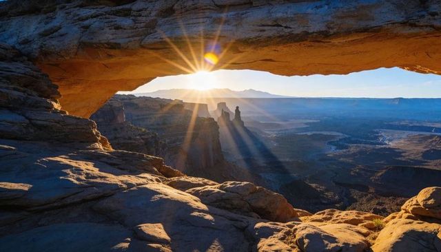 Sunburst framing mesa arch over canyonlands spires at sunrise, golden rock ledge wide view