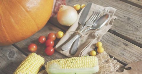 Rustic autumn harvest table with partly husked corn pumpkin cherry tomatoes and tied cutlery