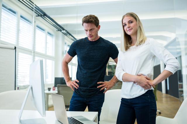 Male and female business executives standing with hands on hips in office