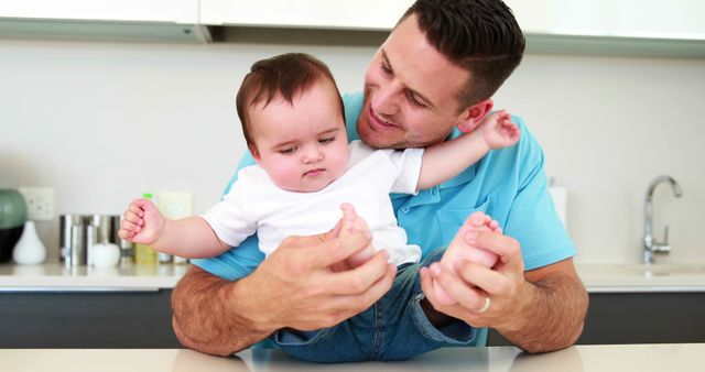 Cheerful father playing with his baby boy at home in the kitchen