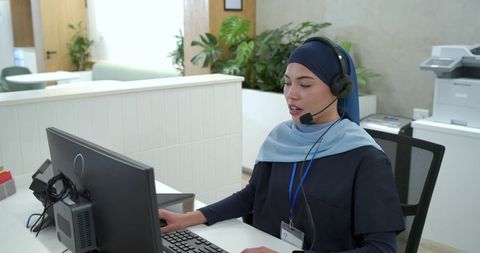 Female receptionist wearing navy hijab assisting callers at modern office reception desk