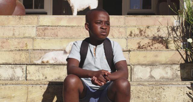 Pensive young boy sitting on outdoor steps with backpack - Download Free Stock Images Pikwizard.com