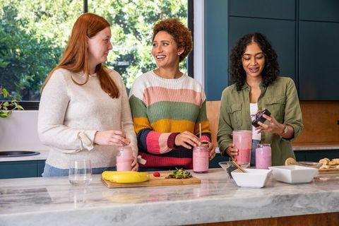 Diverse Women Preparing Fresh Pink Smoothies Together in Modern Kitchen