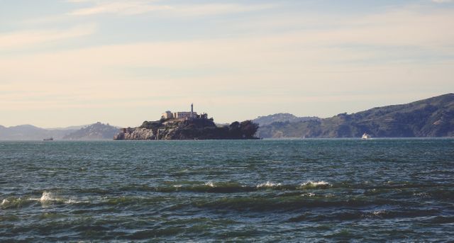 Historic Alcatraz Island is depicted surrounded by calm ocean waters under a clear sky. Known for its notorious prison, Alcatraz serves as a significant landmark and tourist attraction. Sunlight adds to the serene ambiance, showcasing the island's distinct infrastructure. Ideal for use in travel articles, history discussions, or websites focused on famous landmarks and scenic views.