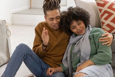 Cozy african american couple sitting on floor leaning on sofa, casual sweaters and jeans