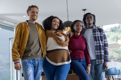 Diverse friends standing together smiling in modern living room with natural light