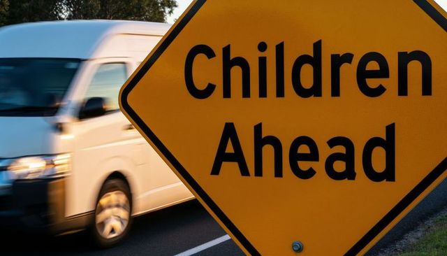 Children ahead warning sign showing passing van and road motion blur evening