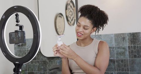 African american woman filming skincare demo with led ring light at bathroom vanity