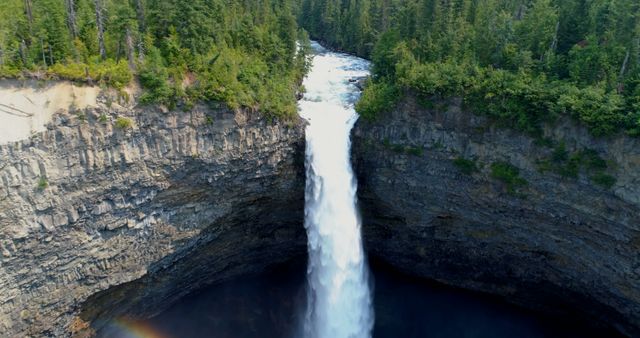 Aerial view of a majestic waterfall cascading down a rugged cliff surrounded by dense forest. The waterfall's powerful flow and the serene natural landscape make it a captivating sight for nature enthusiasts and photographers.