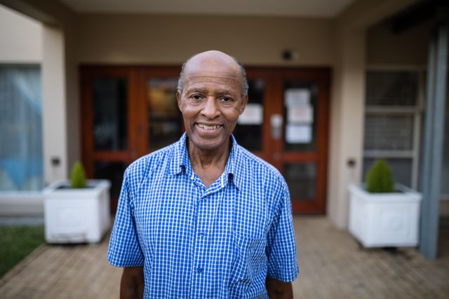 Senior man standing outside a nursing home, smiling warmly. Ideal for use in healthcare, senior living, retirement community promotions, and aging lifestyle content. Highlights themes of happiness, wellbeing, and independent living in older adults.