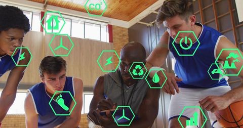 Coach strategizing with basketball team in gym huddle, sustainability energy icons overlay