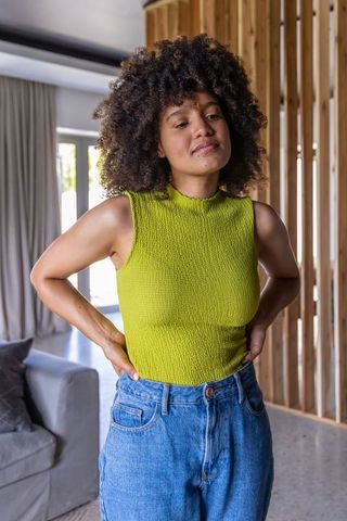 Relaxed african american woman standing hands on hips wearing lime-green top and jeans