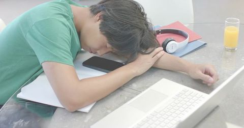 Tired asian student napping on glass table with laptop, smartphone and headphones, study burnout