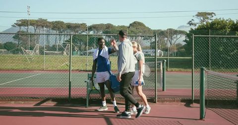 Tennis teammates walking off court carrying rackets and gear while greeting each other