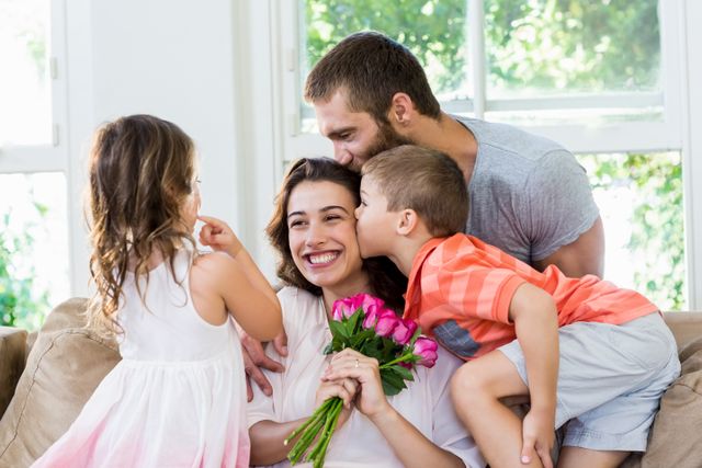 Happy mother receiving bunch of flowers from her family in living room
