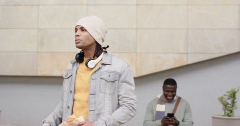 Urban friends walking with headphones and smartphone, holding takeaway bag, casual streetwear