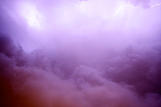 Purple sky filled with thick clouds and a lightning bolt in the distance. Usage ideas include weather-related content, dramatic background for designs, atmospheric elements for mood-setting in videos, inspiration for artists and photographers.