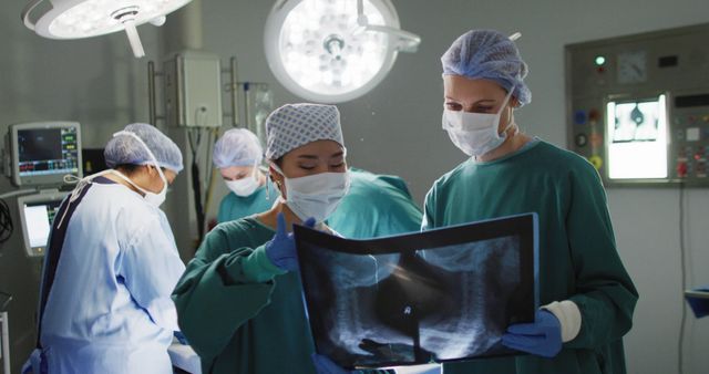 Image of two diverse female surgeons discussing x-ray in operating theatre. Hospital, medical and healthcare services.