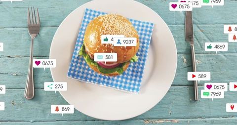 Social media reaction bubbles around sesame burger on rustic turquoise table with gingham napkin