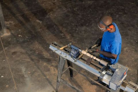 Artisan turning wooden spindle on lathe in workshop showing precision woodworking