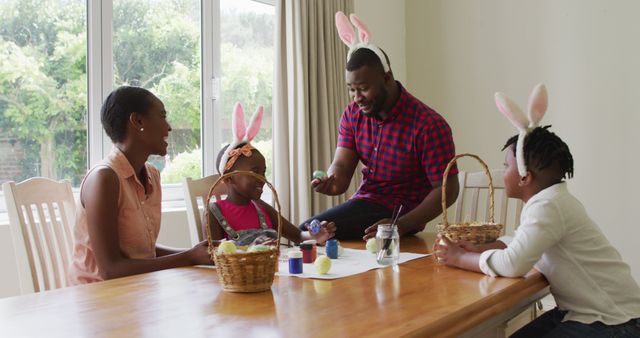 Family members sitting at table and engaging in Easter craft activities, wearing bunny ears. Ideal for use in articles or ads highlighting family bonding, holiday celebrations, and creative activities with children during Easter.