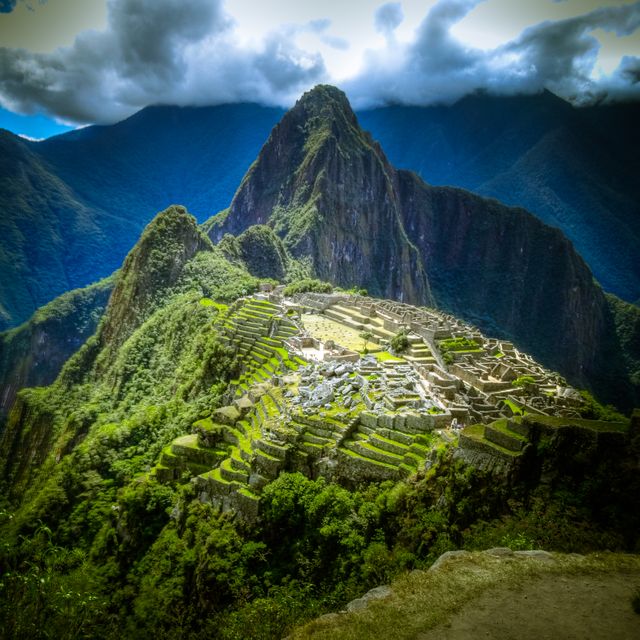 This awe-inspiring shot captures the ancient Inca ruins of Machu Picchu nestled in lush green mountains with a dramatic cloud-strewn sky. Ideal for use in travel magazines, tourism promotions, educational materials about historical sites, or as an inspirational photograph for adventure seekers.
