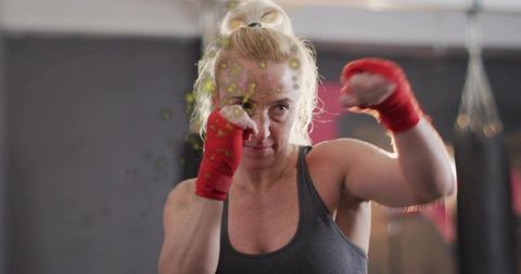 Blonde woman punching in boxing gym wearing red hand wraps and gray tank, intense training